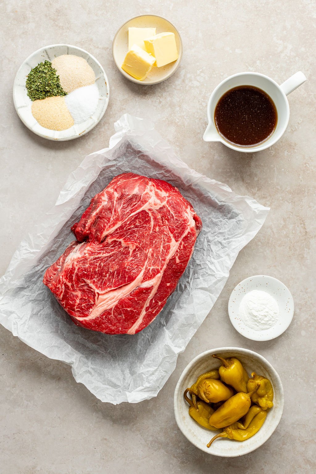 Overhead shot of the following ingredients: raw chuck roast, pepperoncini, broth, butter, cornstarch, dried parsley, garlic powder, onion powder, and salt.