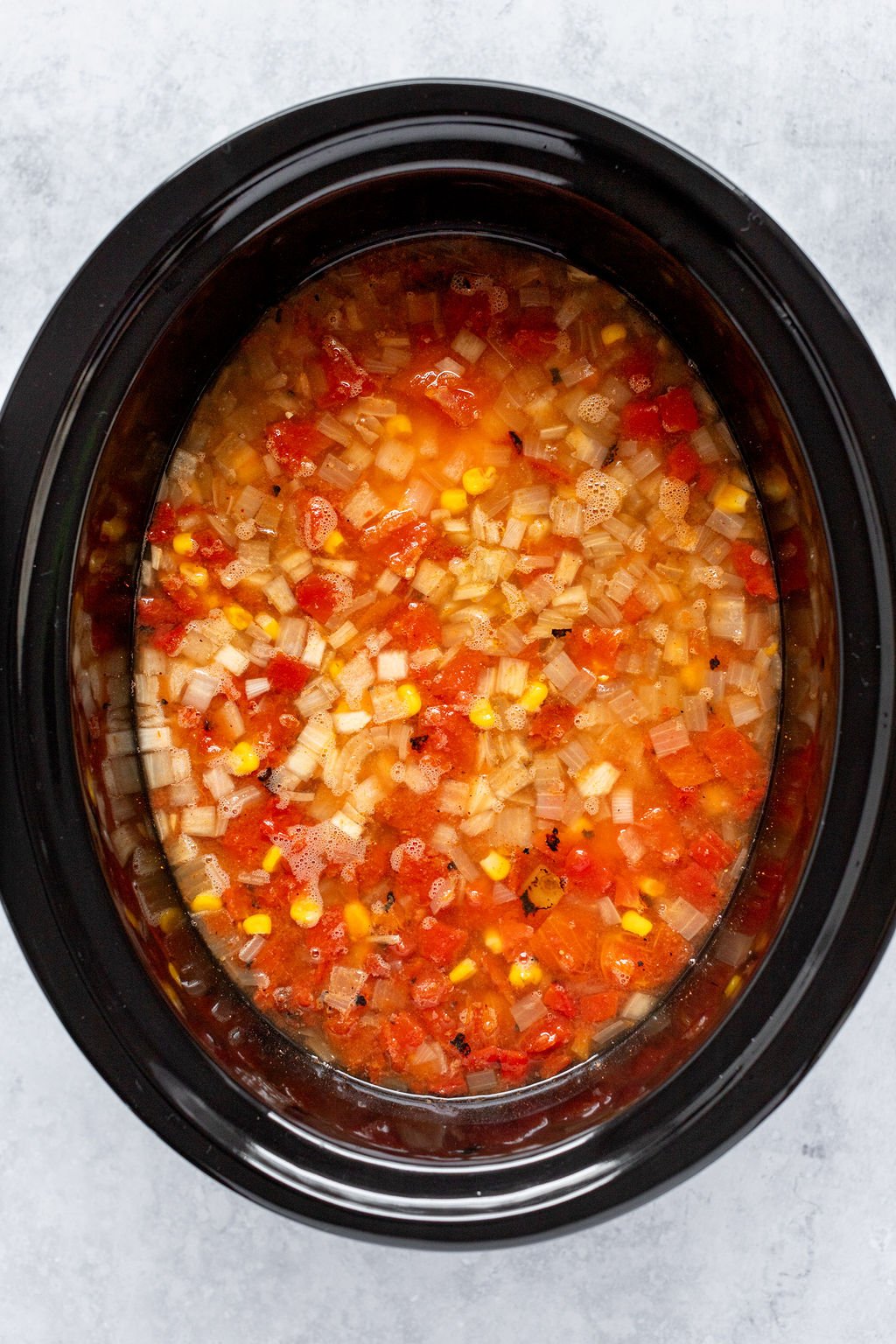 Overhead shot of a slow cooker with broth, diced tomatoes, diced onion, and corn.