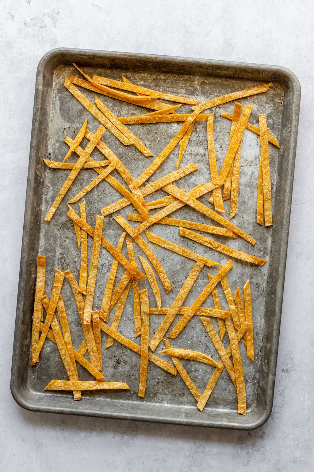 Overhead image of corn tortilla strips on a baking sheet.