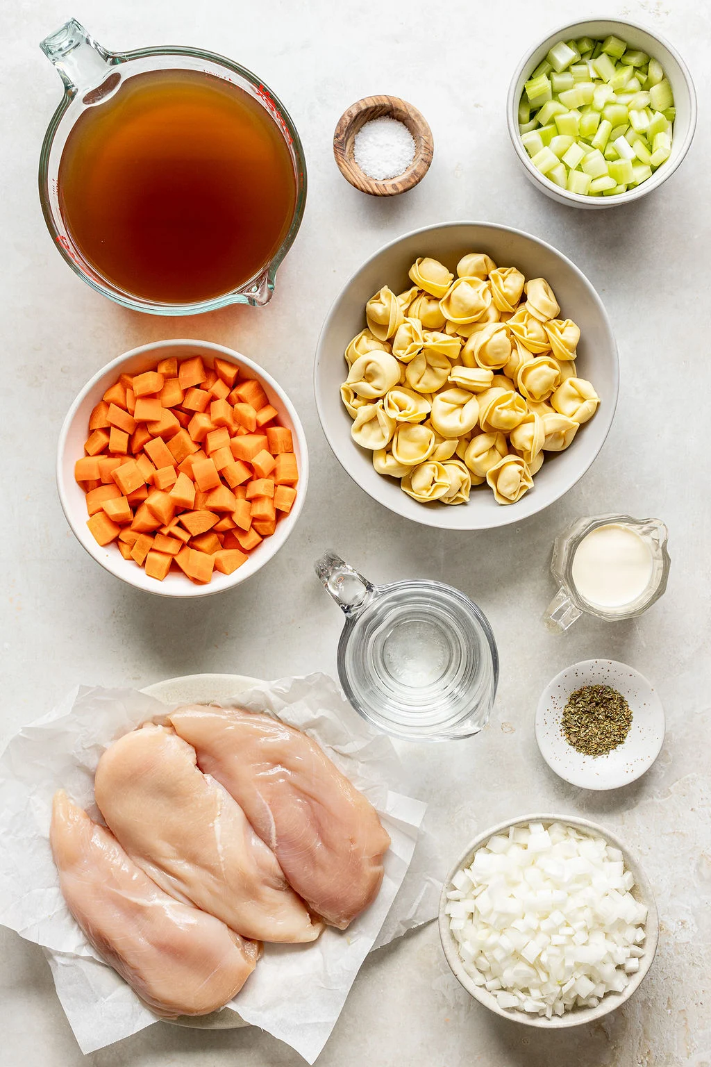 Overhead shot of the following ingredients: broth, salt, diced celery, tortellini, cream, pepper, water, diced onion, chicken breasts, and diced carrots.