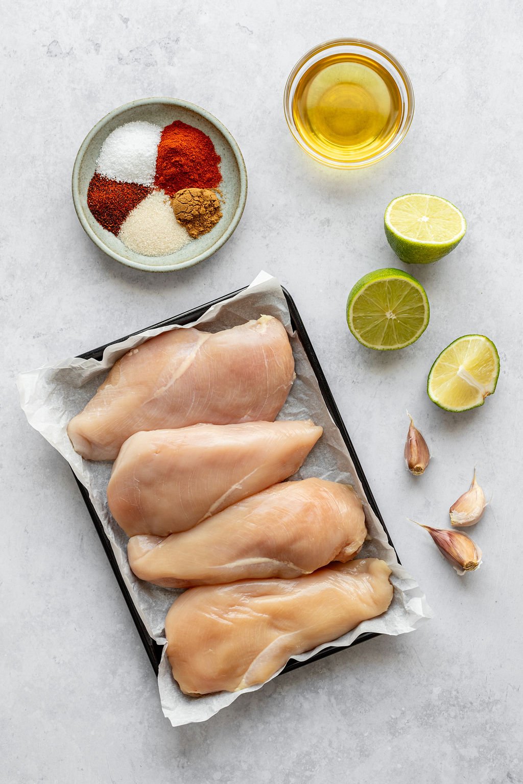 Overhead shot of the following ingredients: raw chicken breasts, spices, oil, lime, garlic.