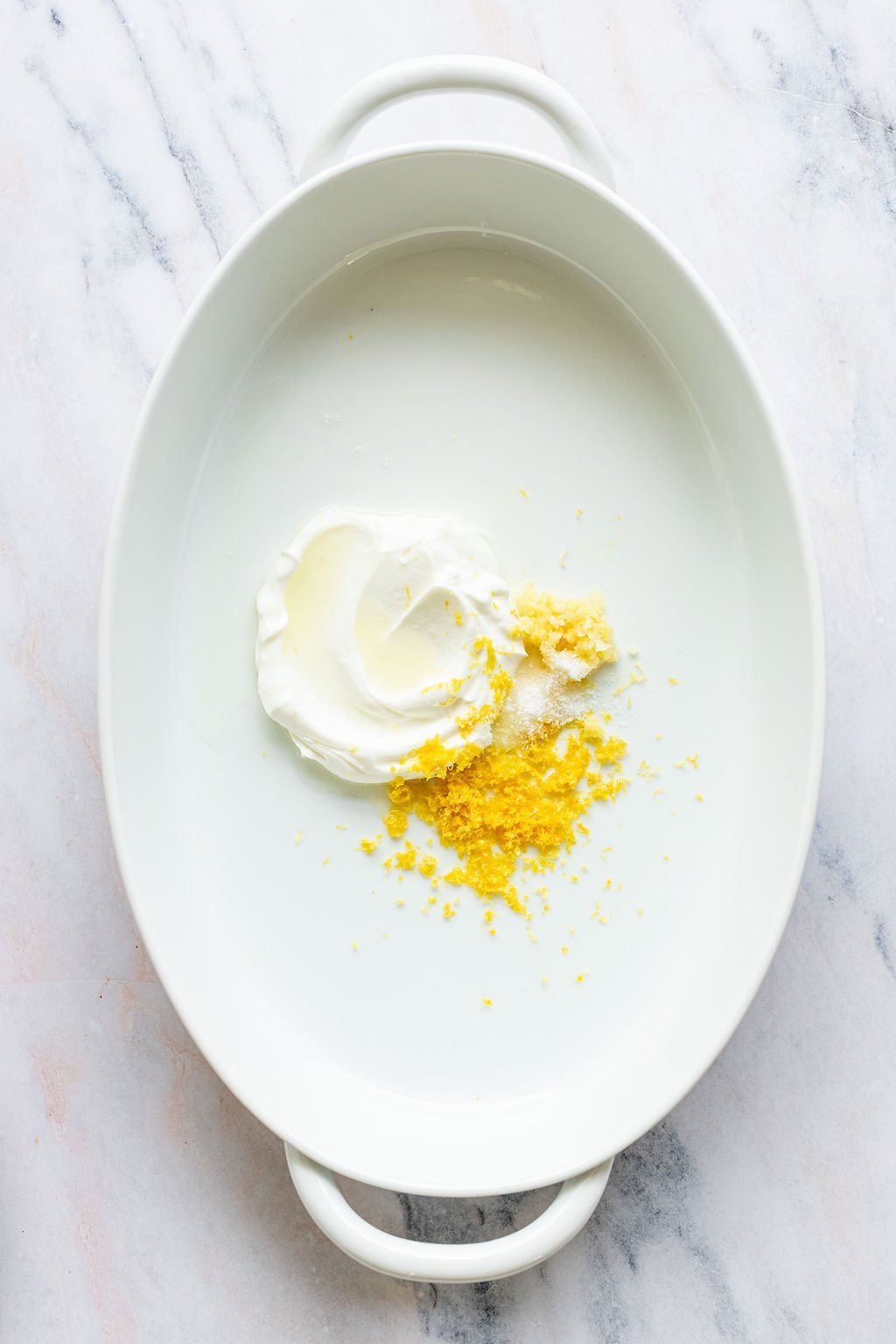 Overhead shot of a white oval baking dish with yogurt and lemon zest.