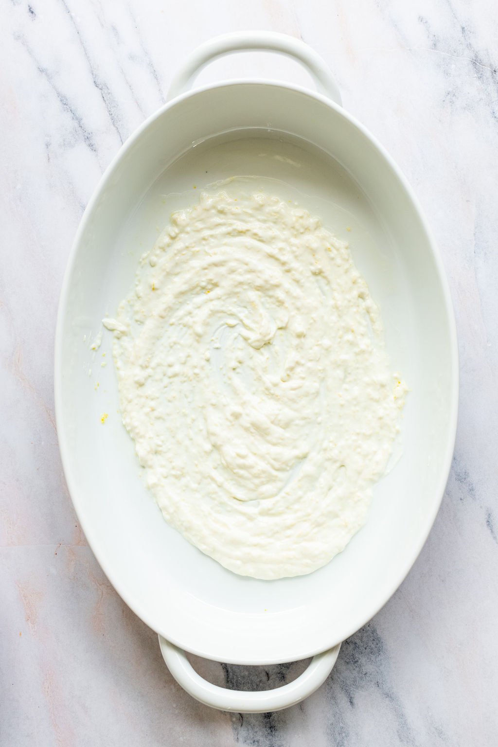 Overhead shot of a white oval baking dish with yogurt mixed with lemon zest.