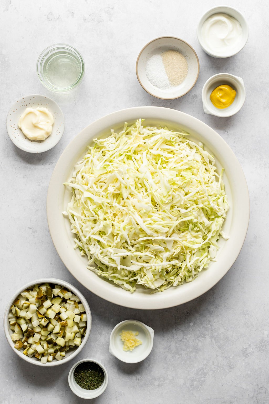 Overhead shot of the following ingredients: shredded cabbage, mayonnaise, vinegar, dill pickles, dried dill, garlic, mustard, Greek yogurt, salt, sugar.