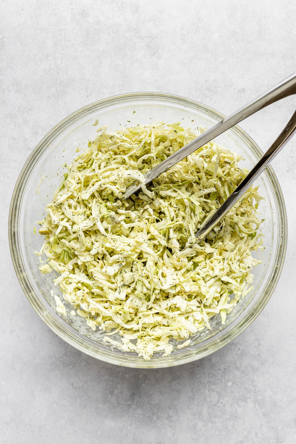 Overhead shot of a large glass bowl with coleslaw and tongs.