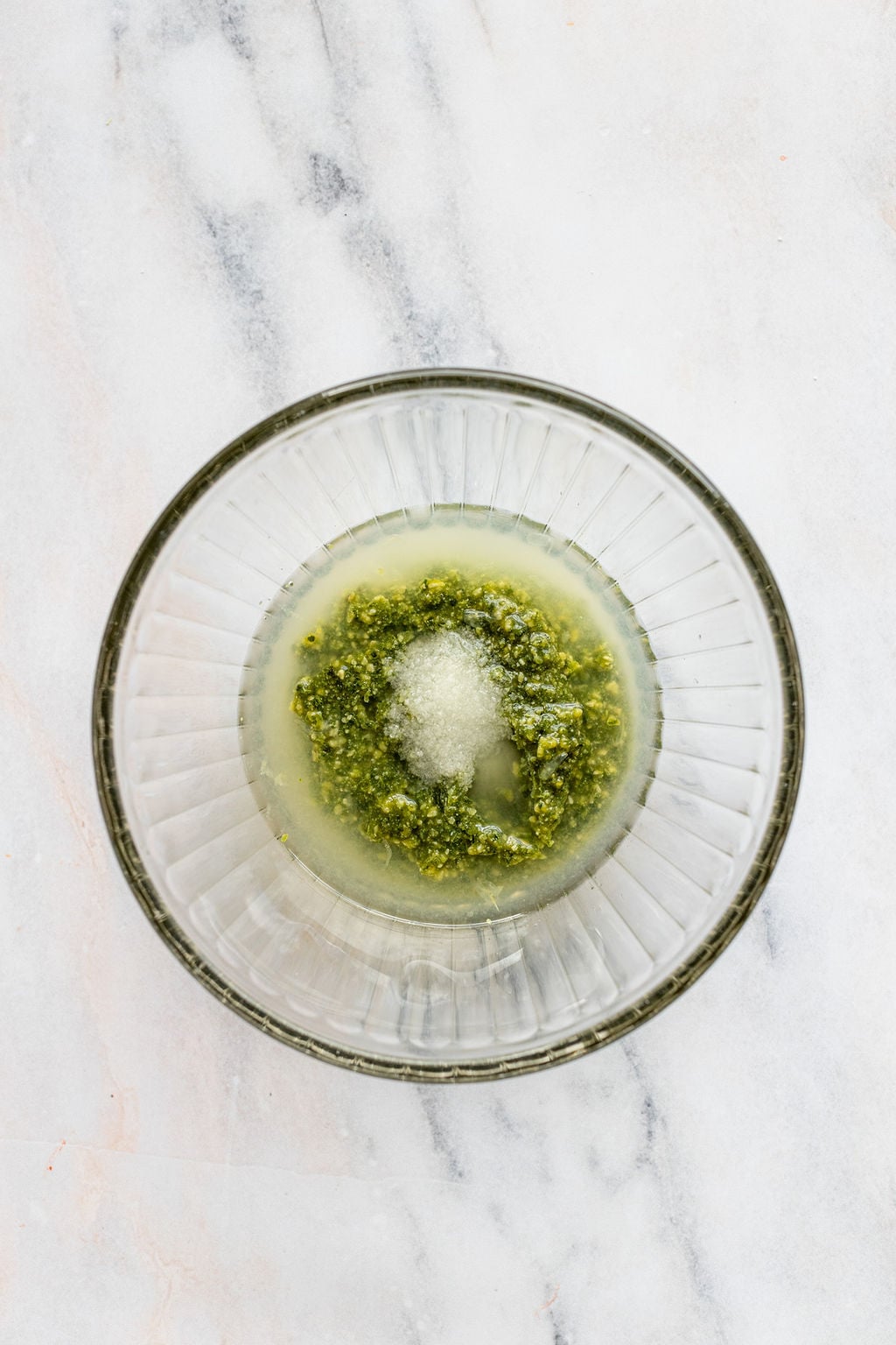 Overhead shot of a glass bowl with pesto, lemon juice, and salt.