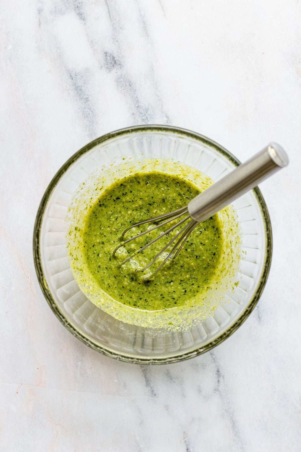 Overhead shot of a glass bowl with green sauce and a whisk.