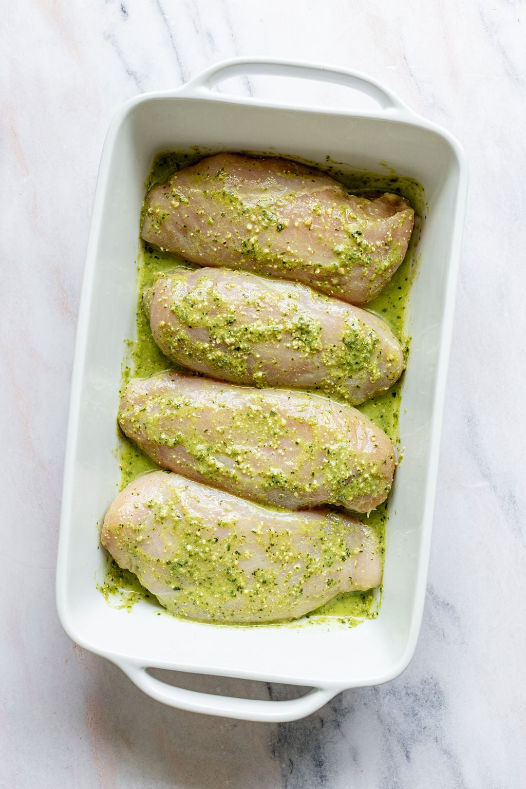 Overhead shot of a white baking dish with chicken breasts covered in green sauce.