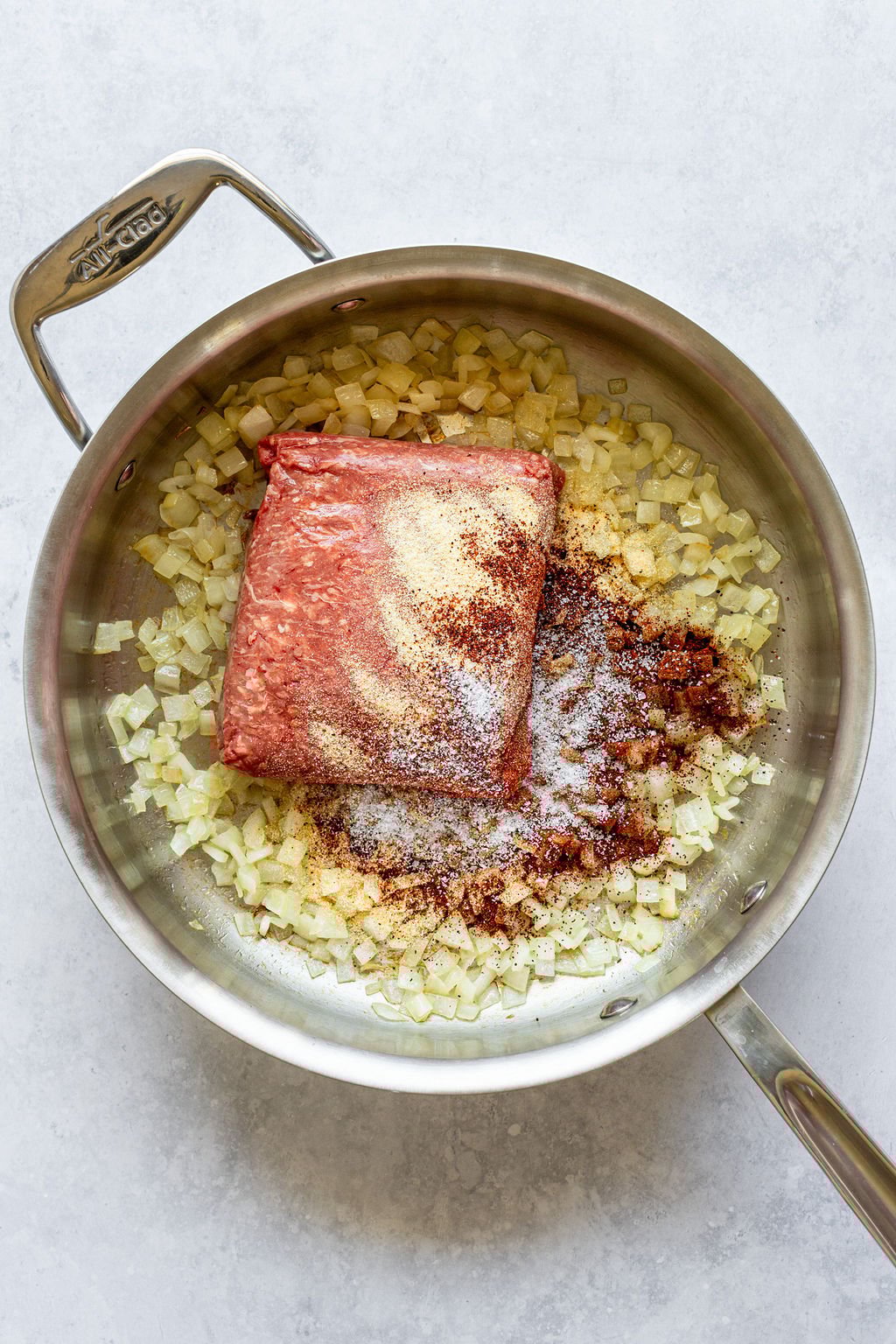 Saucepan with cooked, diced onion, chili powder, ground beef, and salt.