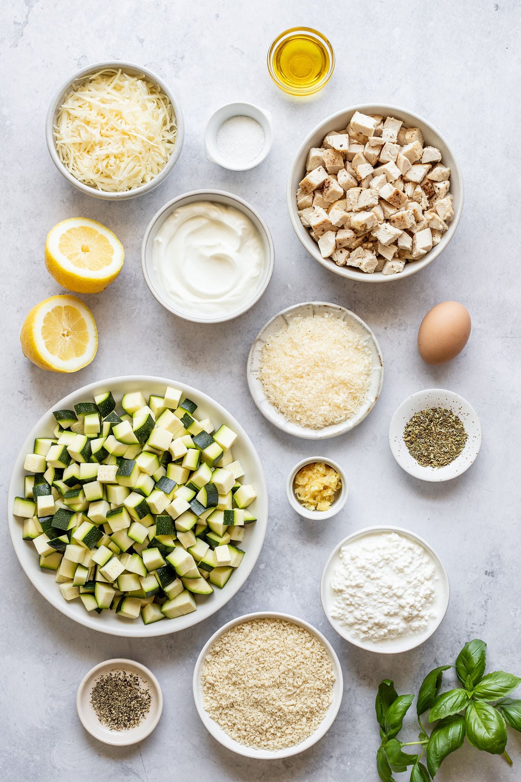 Chopped zucchini, lemons, shredded cheese, salt, oil, diced chicken, breadcrumbs, pepper, minced garlic, dried herbs, egg, cottage cheese, and fresh basil.