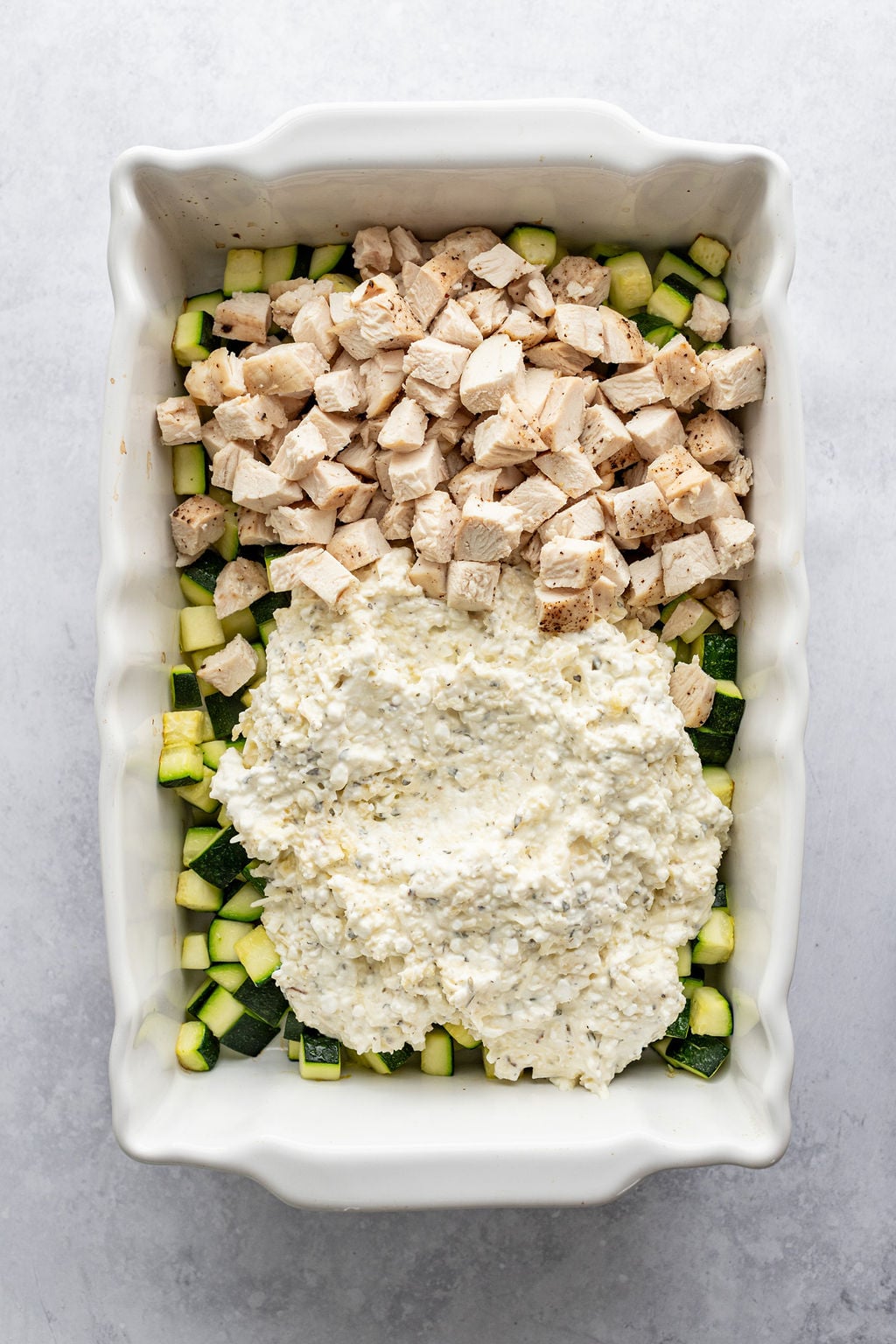White baking dish with diced zucchini, diced chicken, and a cottage cheese mixture.