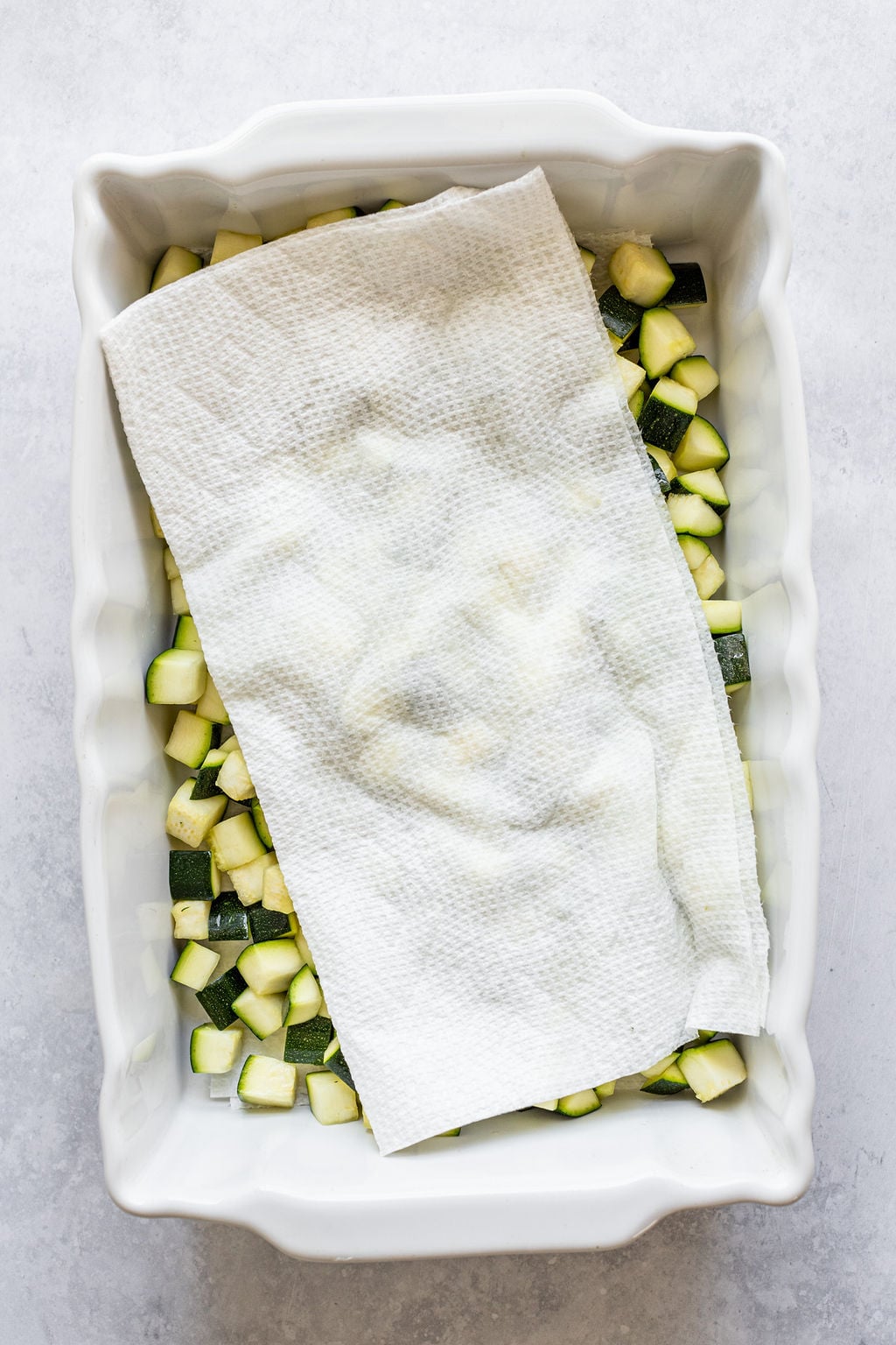 White baking dish with diced zucchini covered with a paper towel.