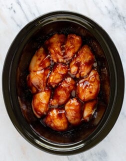Overhead shot of a slow cooker with raw chicken thighs covered in a red sauce.
