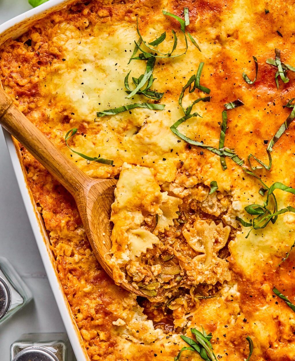 A wooden spoon in a casserole dish filled with pasta, cheesy ground beef, and zucchini.