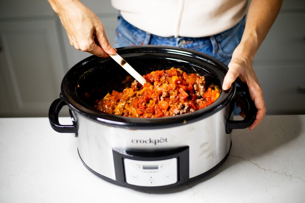 Woman stirring pumpkin chili in a slow cooker with a wooden spoon.