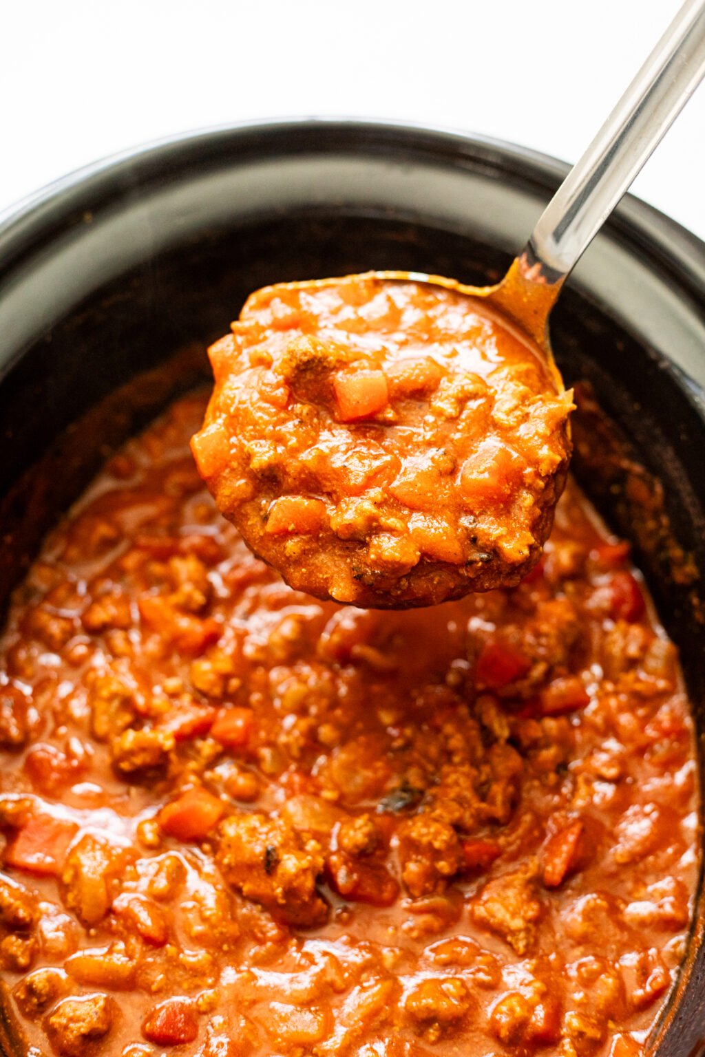 Ladle of pumpkin chili in a black slow cooker.
