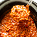 Ladle of pumpkin chili in a black slow cooker.