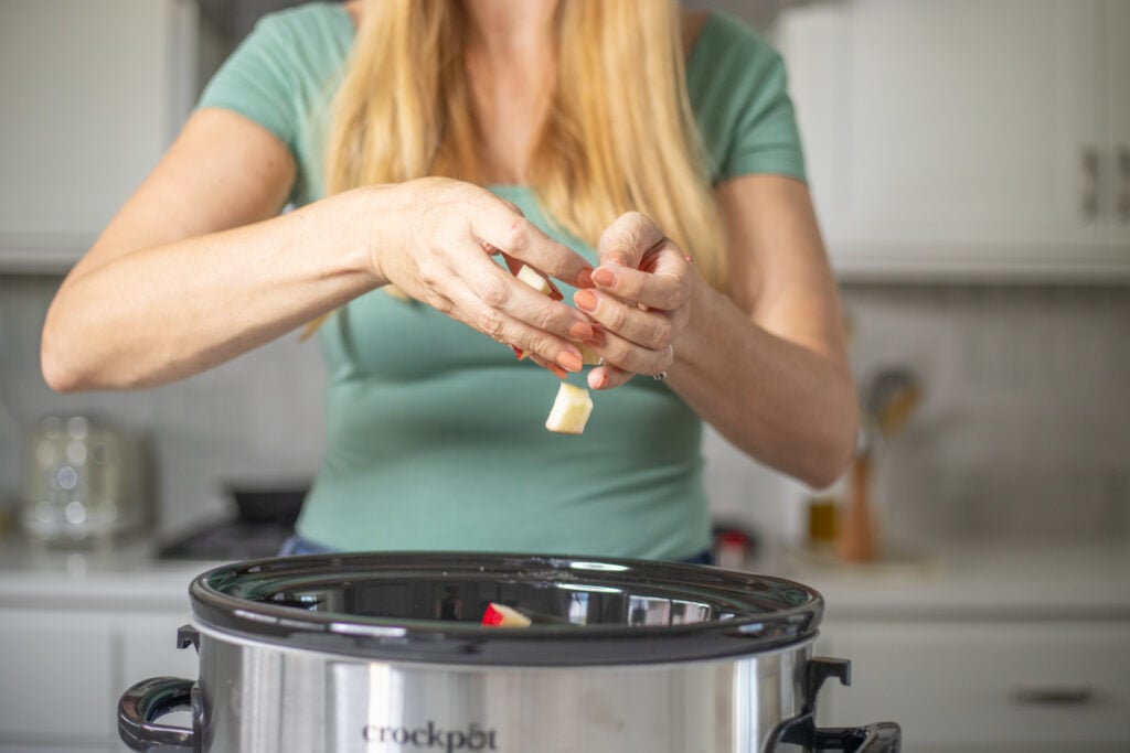 Person adding diced apple to a slow cooker.