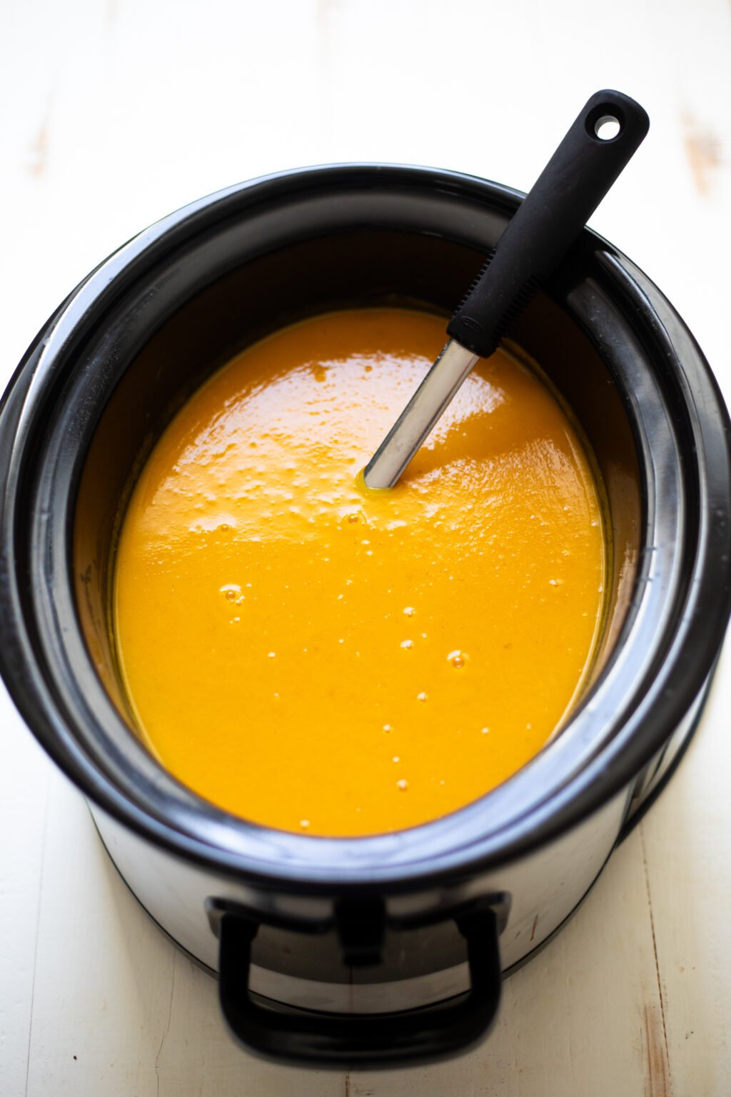 Ladle sitting in butternut squash soup in a black slow cooker.