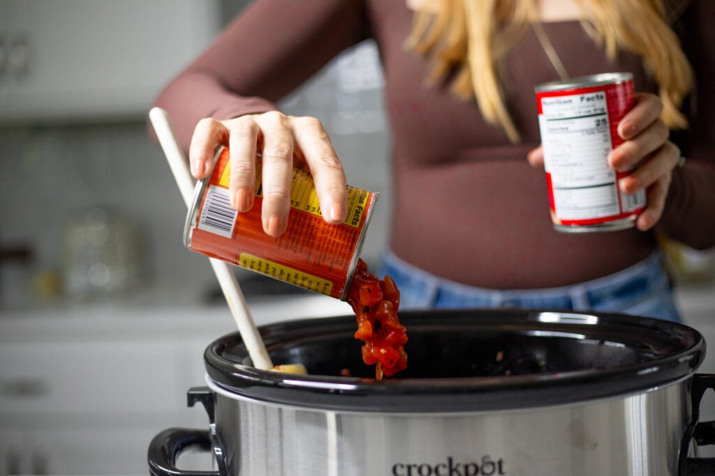 Person pouring can of tomatoes into a slow cooker.