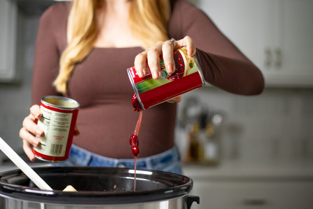 Person pouring can of beans into a slow cooker.