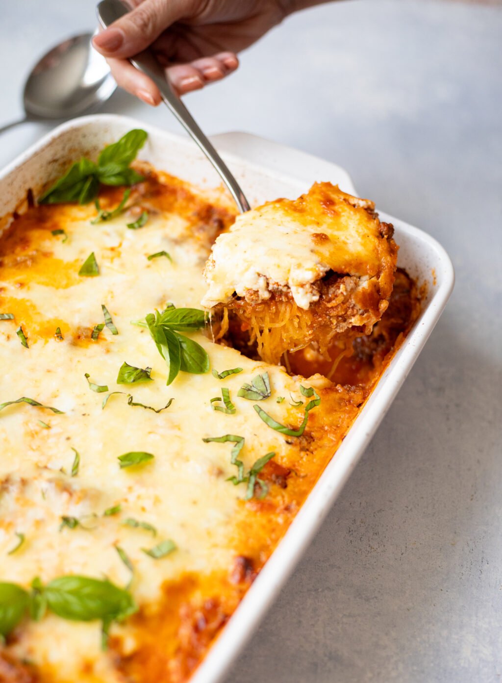 Taking a spoonful of spaghetti squash casserole out of a white baking dish.