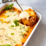 Taking a spoonful of spaghetti squash casserole out of a white baking dish.