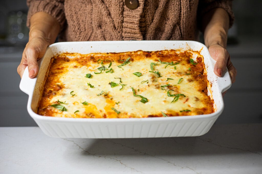 Person holding a spaghetti squash casserole topped with basil in a white baking dish.