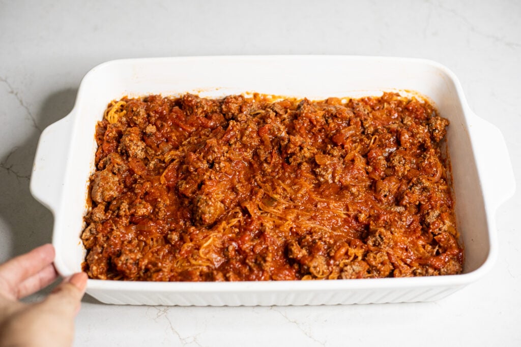 Red sauce, ground beef, and spaghetti squash in a white baking dish.