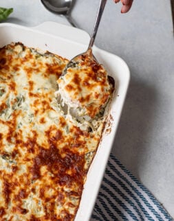Close up of spinach artichoke casserole in a white baking dish with a spoon.