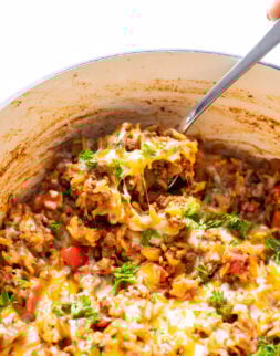 Close-up of a spoon in a pot with a rice, beef, pepper, and cheese casserole.