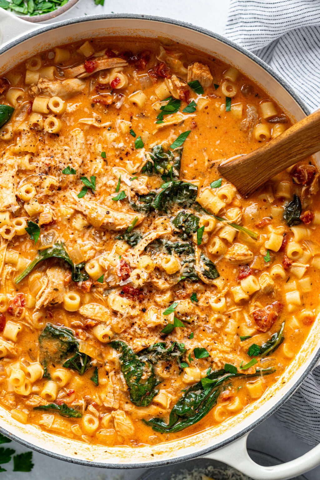 A large white pot filled with creamy tomato soup with pasta, baby spinach, and shredded chicken. 
