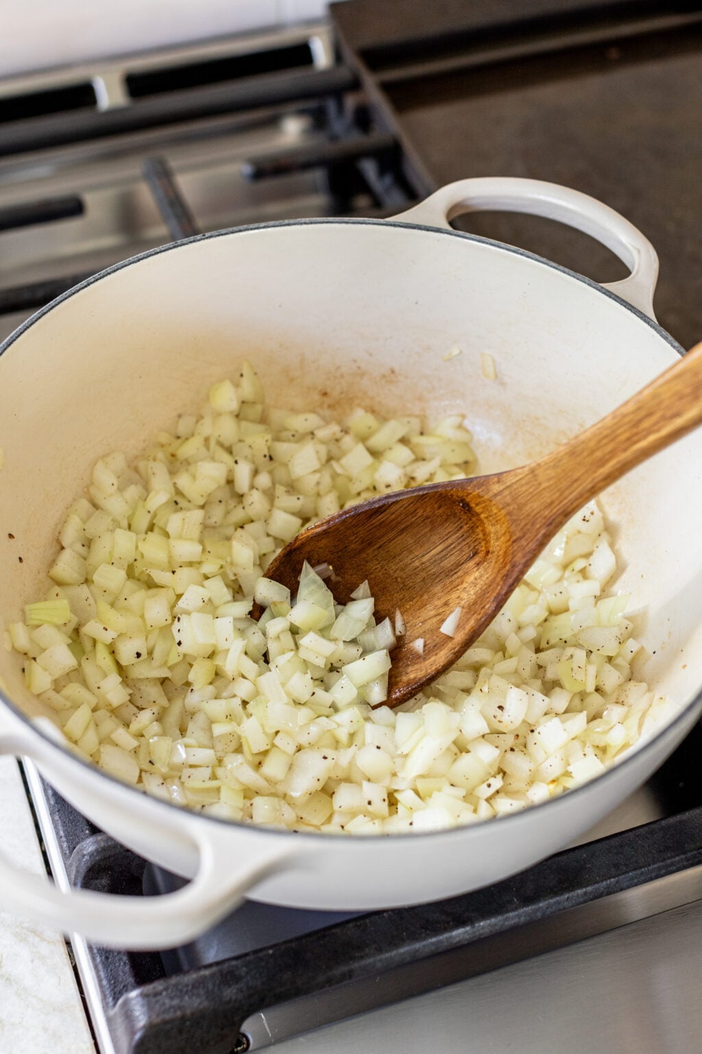 A wooden spoon stirring diced onions in a large pot.