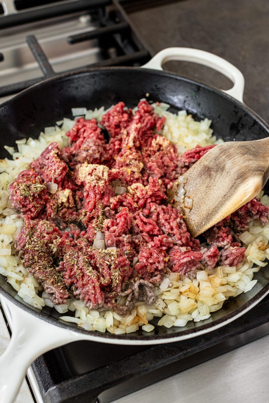 Diced onions and ground beef cooking in a skillet on a stove. 