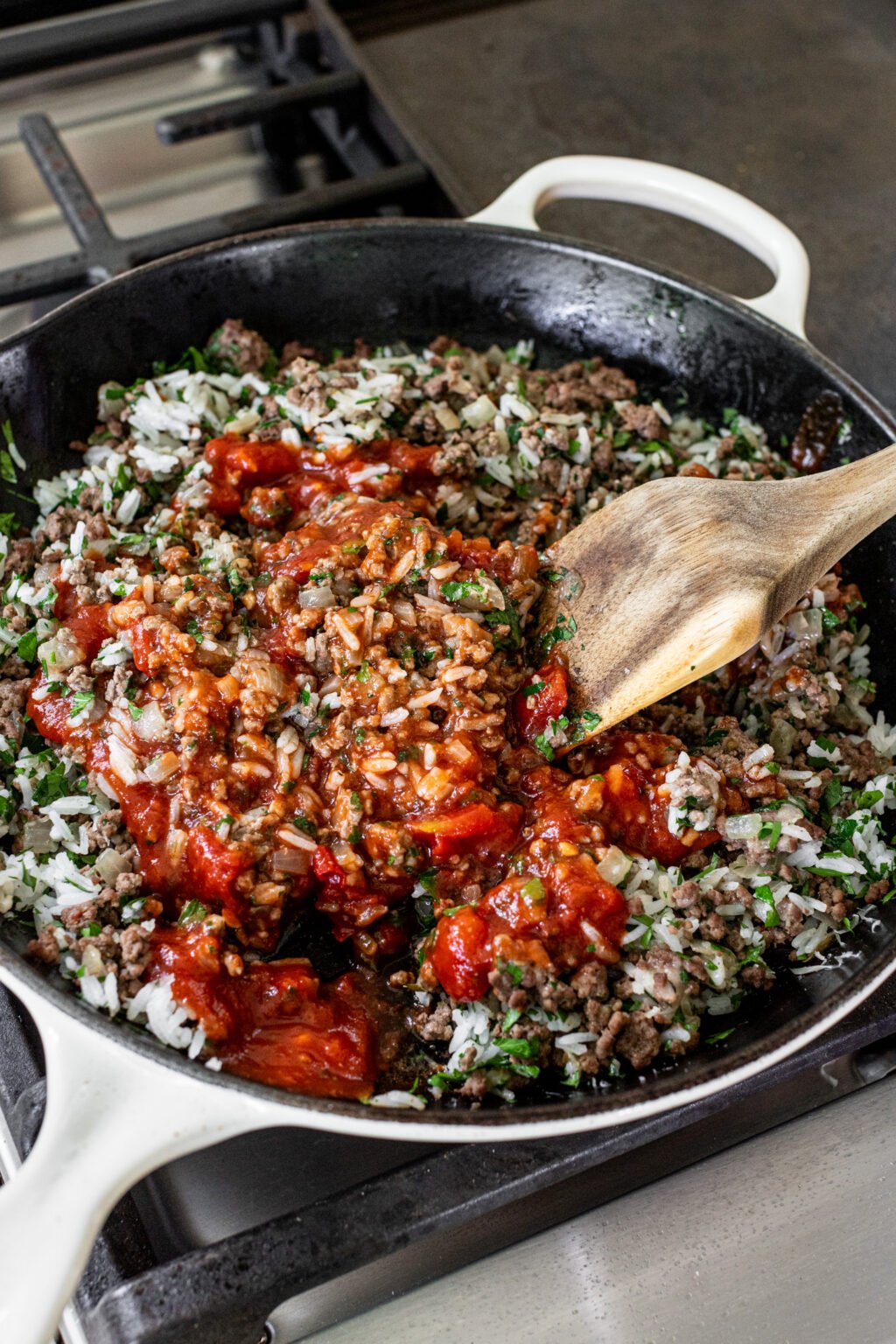 Cooked onions, browned ground beef, and chopped herbs in a skillet.