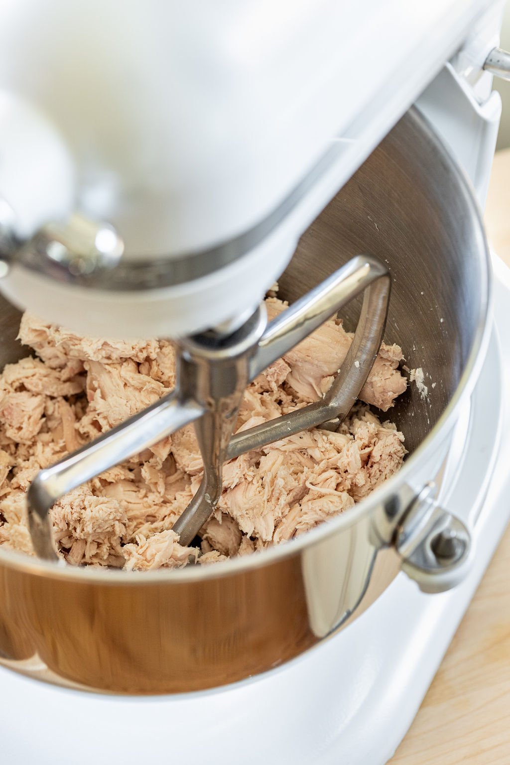 Cooked chicken being shredded in a stand mixer.