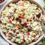 A large bowl of creamy chicken salad topped with diced apples, celery, dried cranberries, and walnuts.