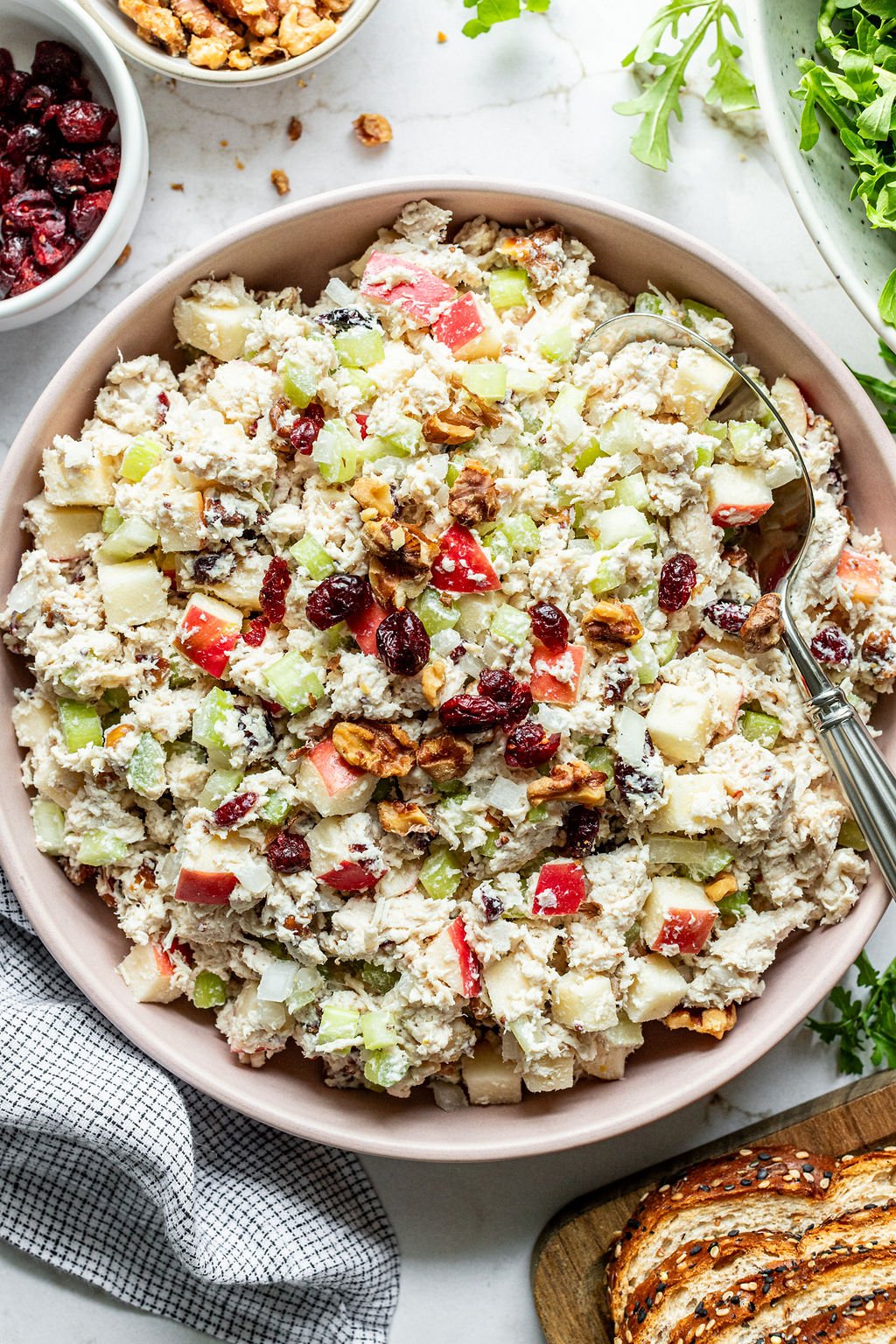 A large bowl of creamy chicken salad topped with diced apples, celery, dried cranberries, and walnuts.
