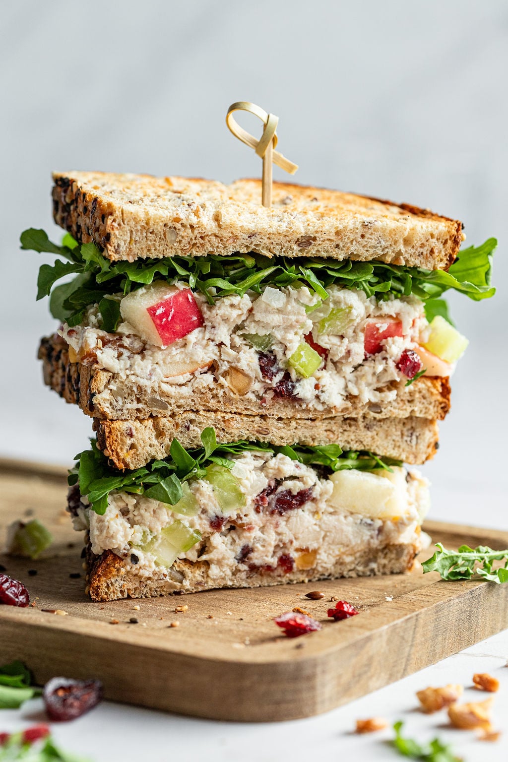 Two thick sandwiches filled with leafy greens and creamy chicken salad stack on top of each other.