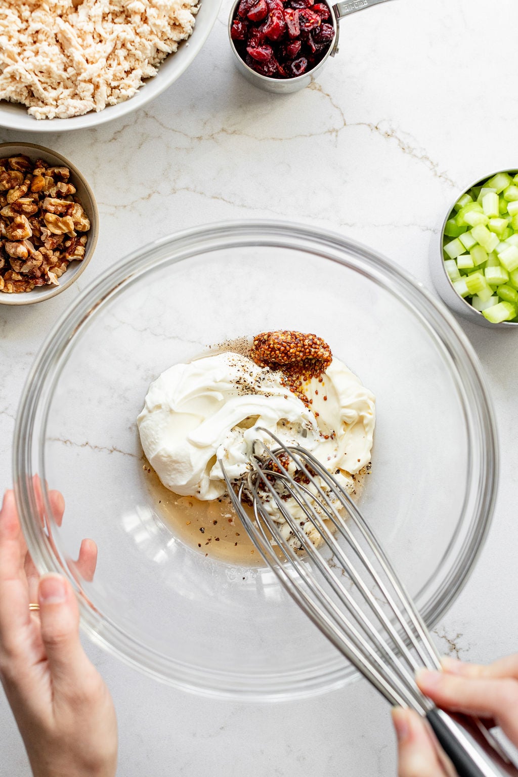 A hand whisking apple cider vinegar, Greek yogurt, mayonnaise, salt, pepper, and mustard in a mixing bowl.