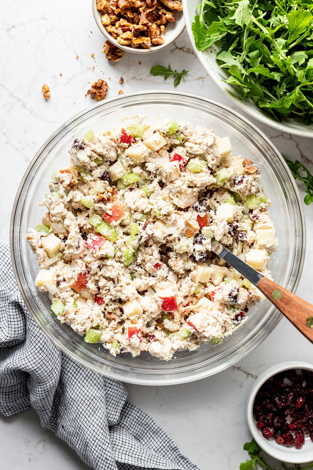 Creamy chicken salad with apples, celery, and cranberries in a glass bowl with a large spoon.