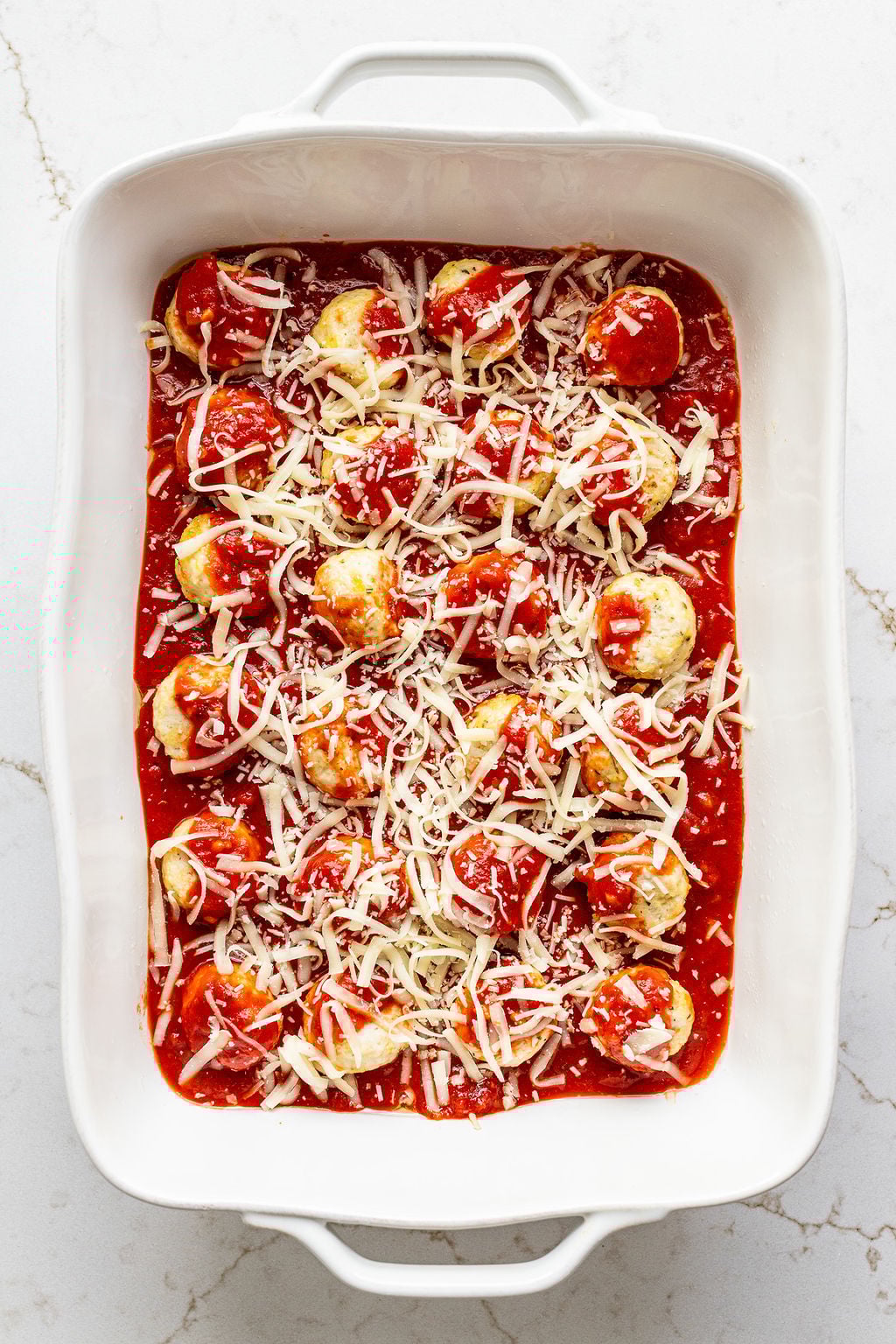Two dozen chicken meatballs covered with tomato sauce and shredded cheese in a casserole dish.