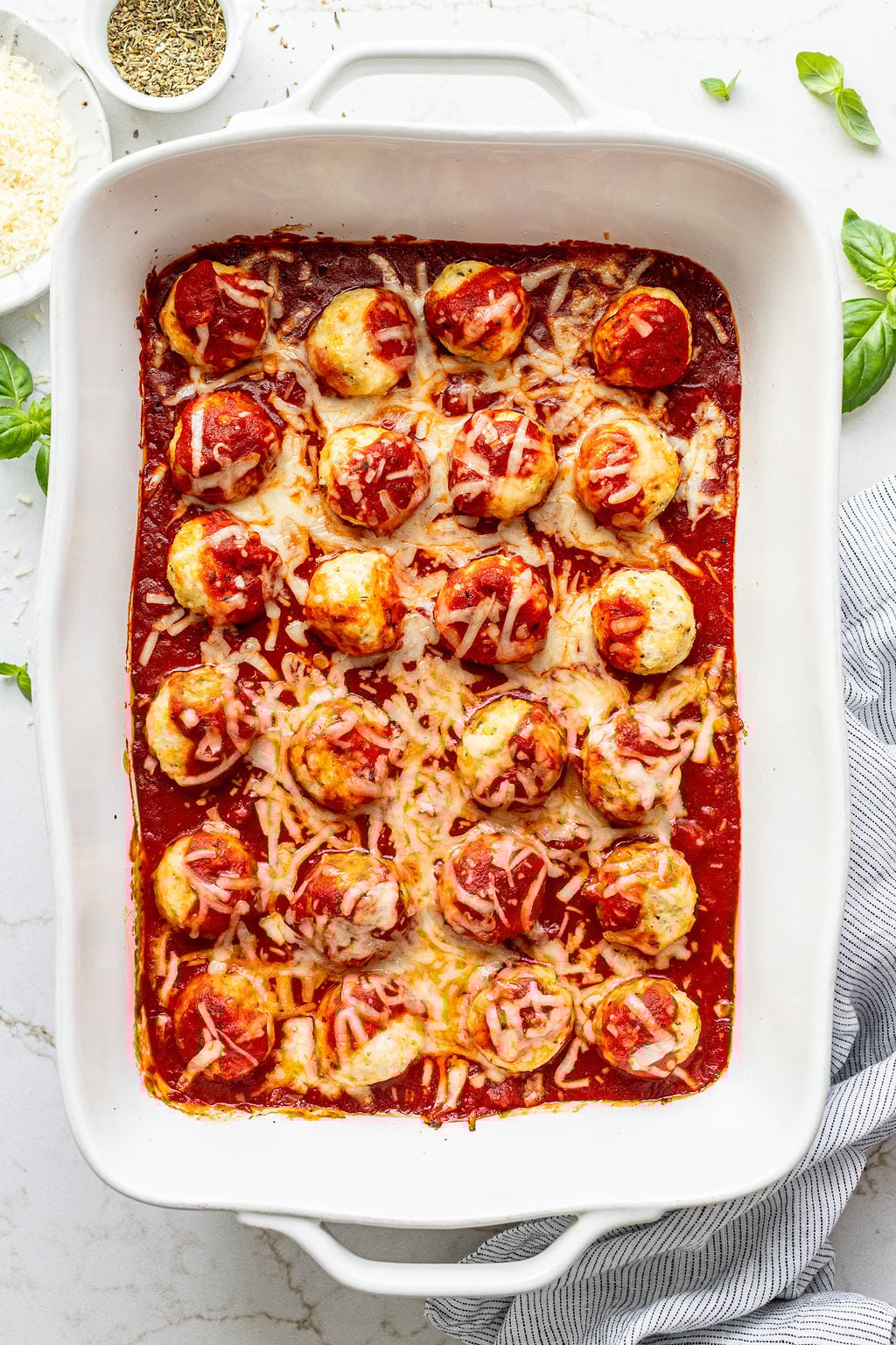 Creamy red sauce and melted cheese on top of baked meatballs in a large casserole dish.