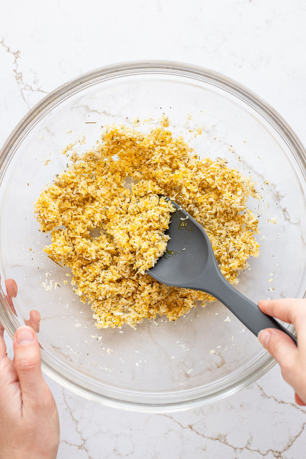 A hand mixing bread crumbs with parmesan and an egg with a large spoon in a mixing bowl.