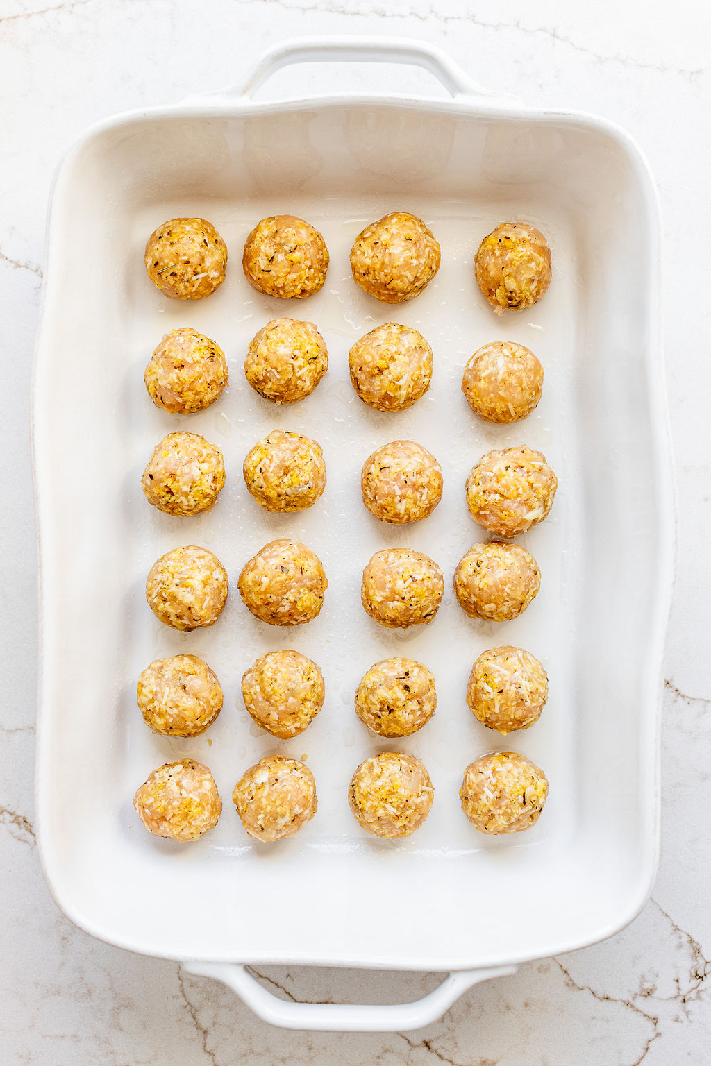 Two dozen round chicken meatballs arranged in rows in a large casserole dish.
