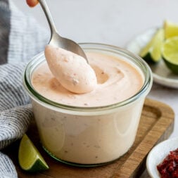 A hand scooping a dollop of creamy orange sauce onto a spoon.