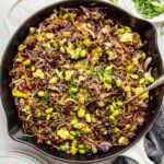 A large skillet with cooked eggs, ground beef, coleslaw mix, and edamame.