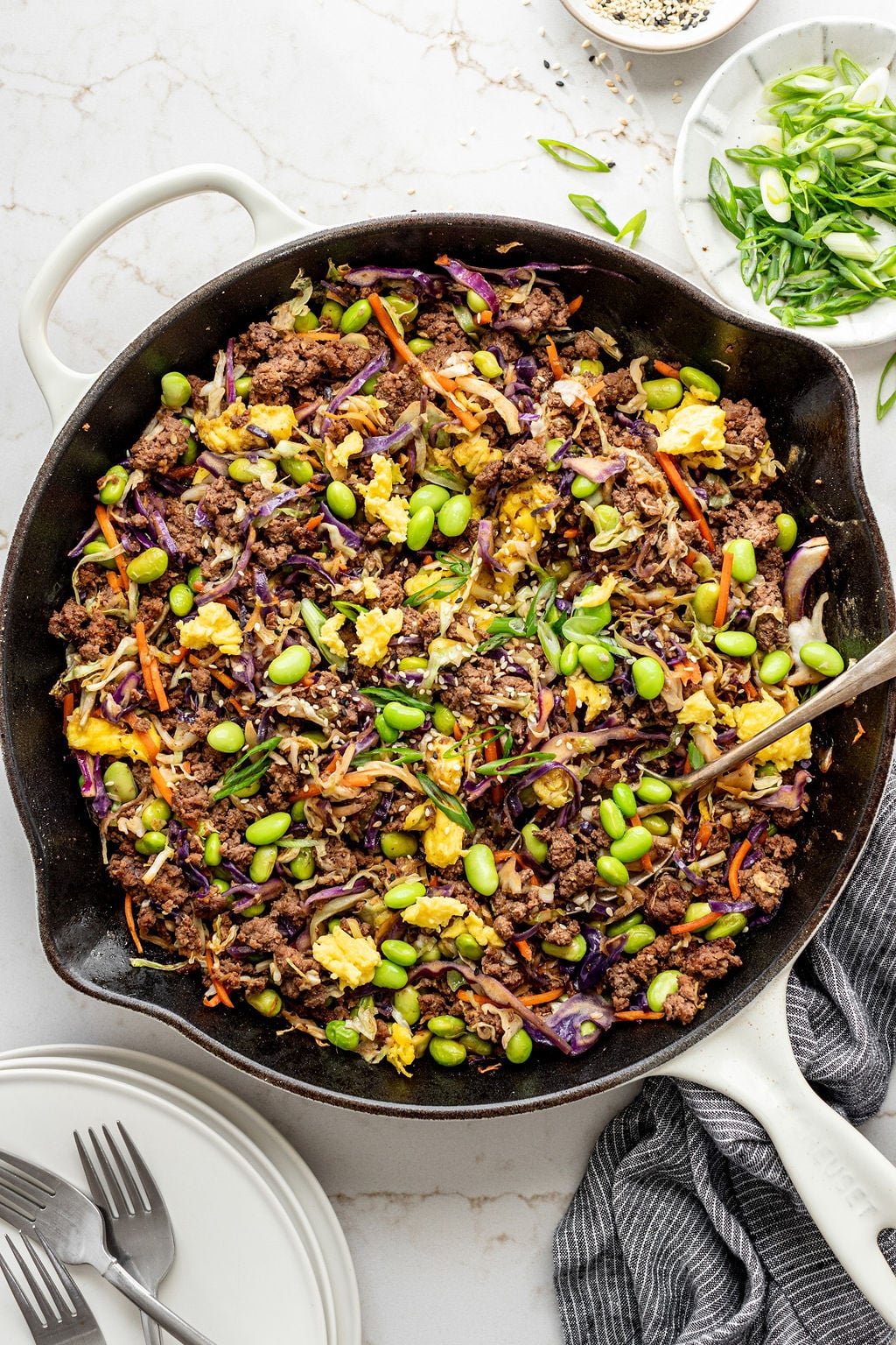 A large skillet with cooked eggs, ground beef, coleslaw mix, and edamame.