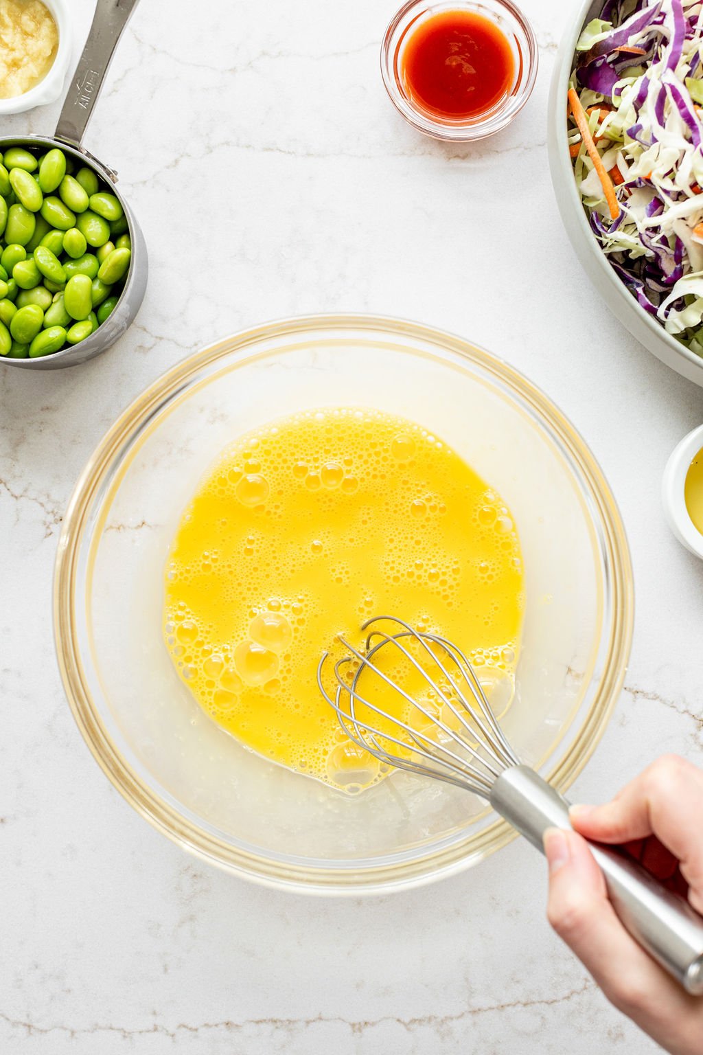 A hand whisking eggs in a large bowl on a marble surface.