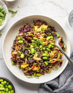 Cooked eggs, ground beef, coleslaw mix, and edamame in a shallow bowl with a fork.
